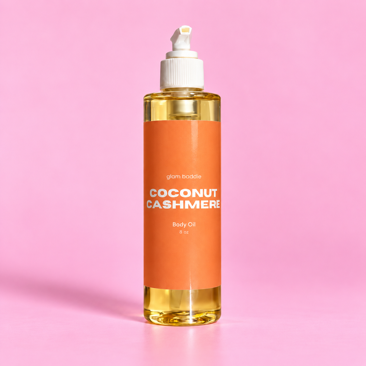 Glam Baddie Coconut Cashmere Body oil 8 oz bottle with orange label on a pink background.